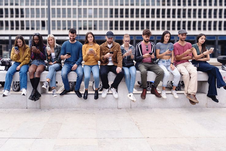 A group of young people looking at their mobile devices. The image illustrates many recipients and to potential to optimize A2P delivery cost for bigger message volumes.